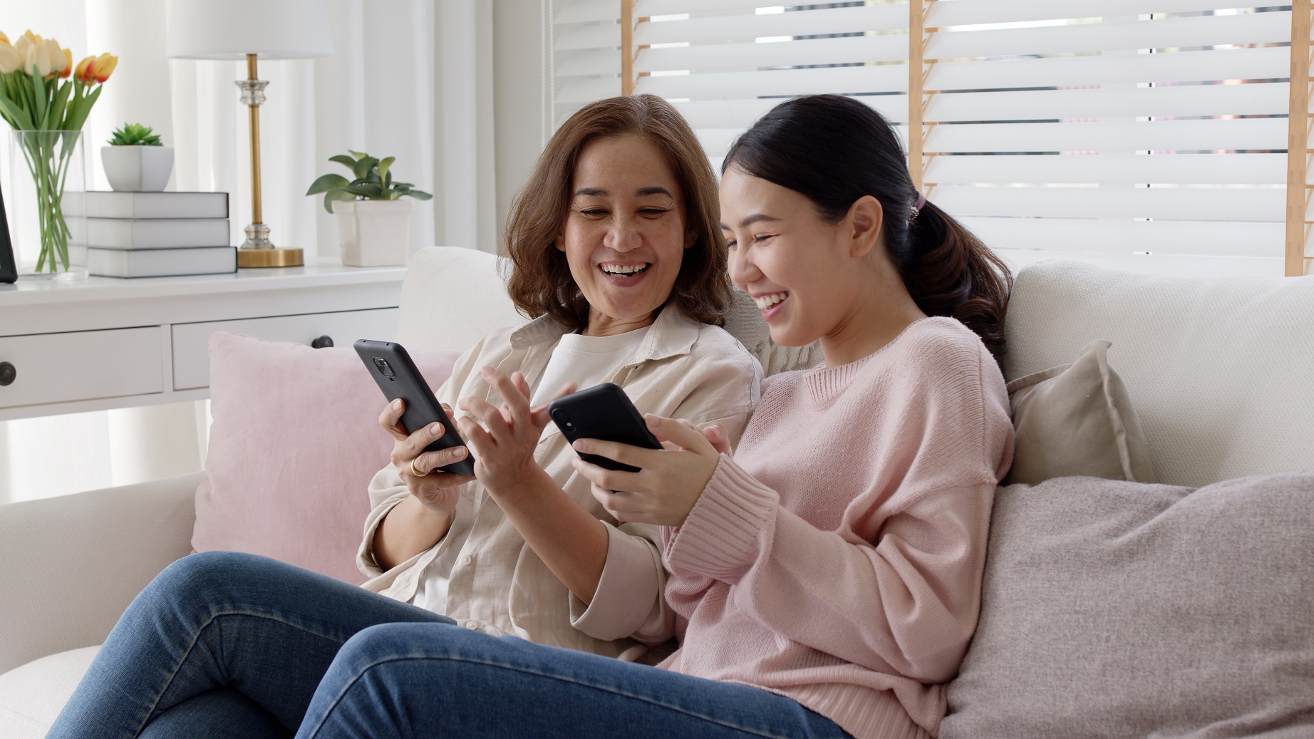 Mother and daughter sitting on sofa smiling while looking at phone
