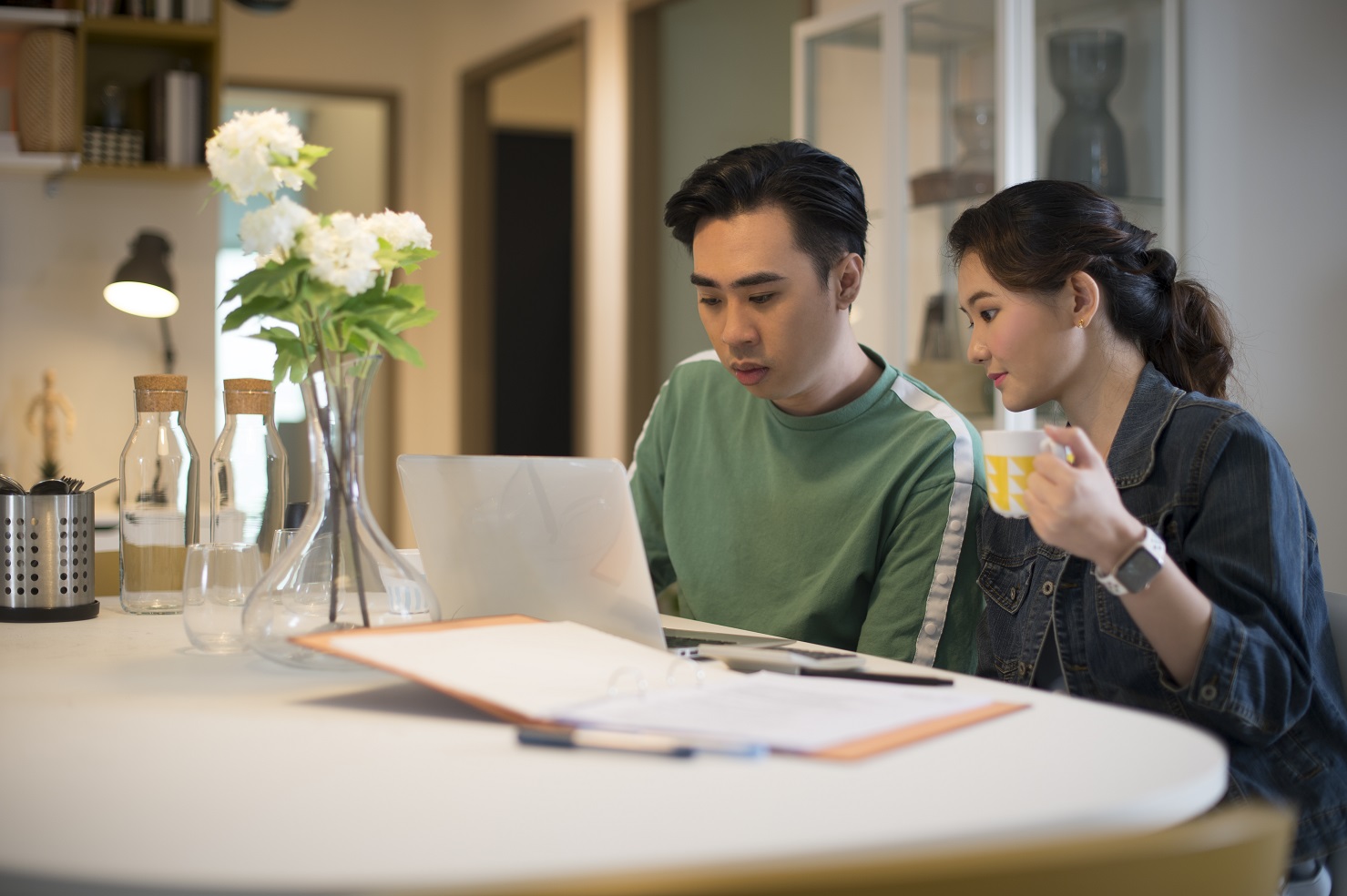 Young couple sitting at the desk planning their home purchase, with their laptop and writing materials