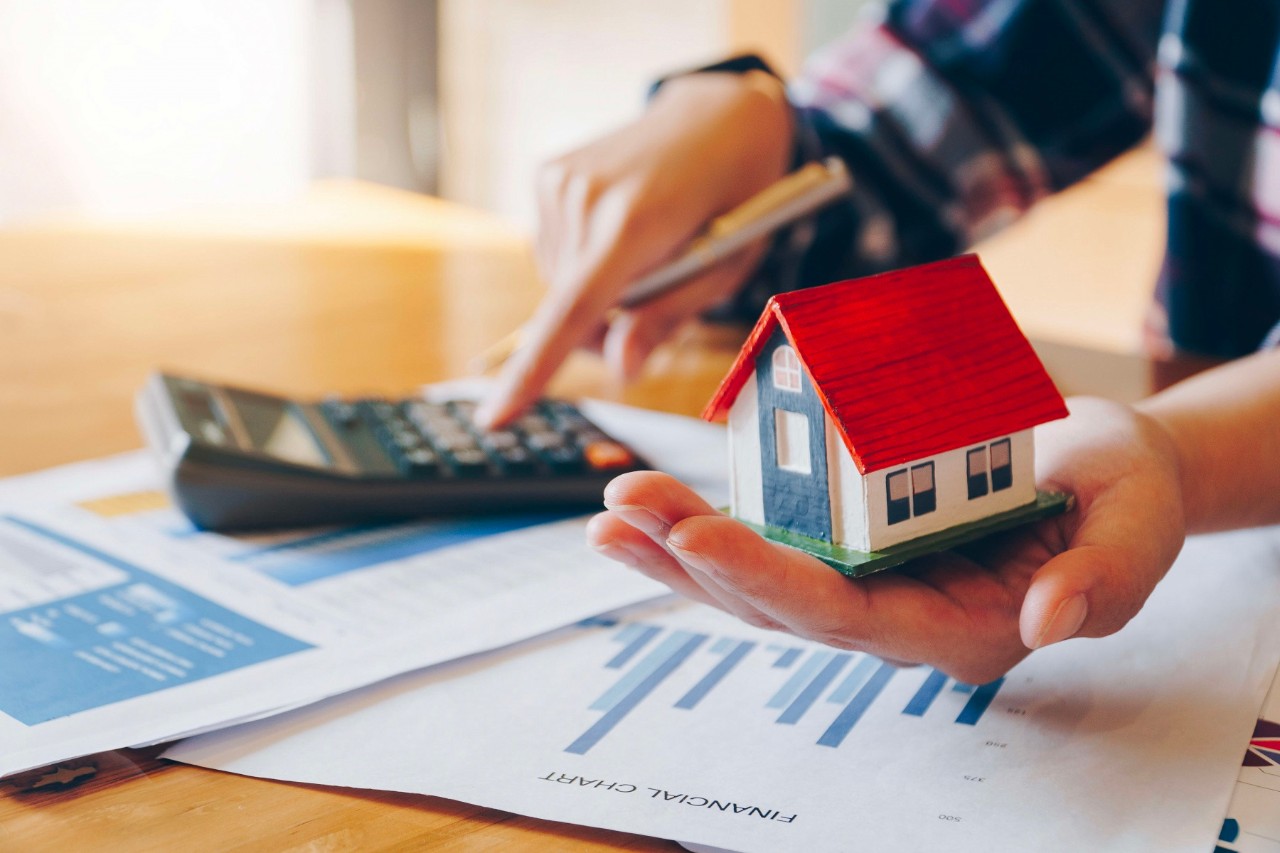 woman holding house model in hand and calculating financial chart