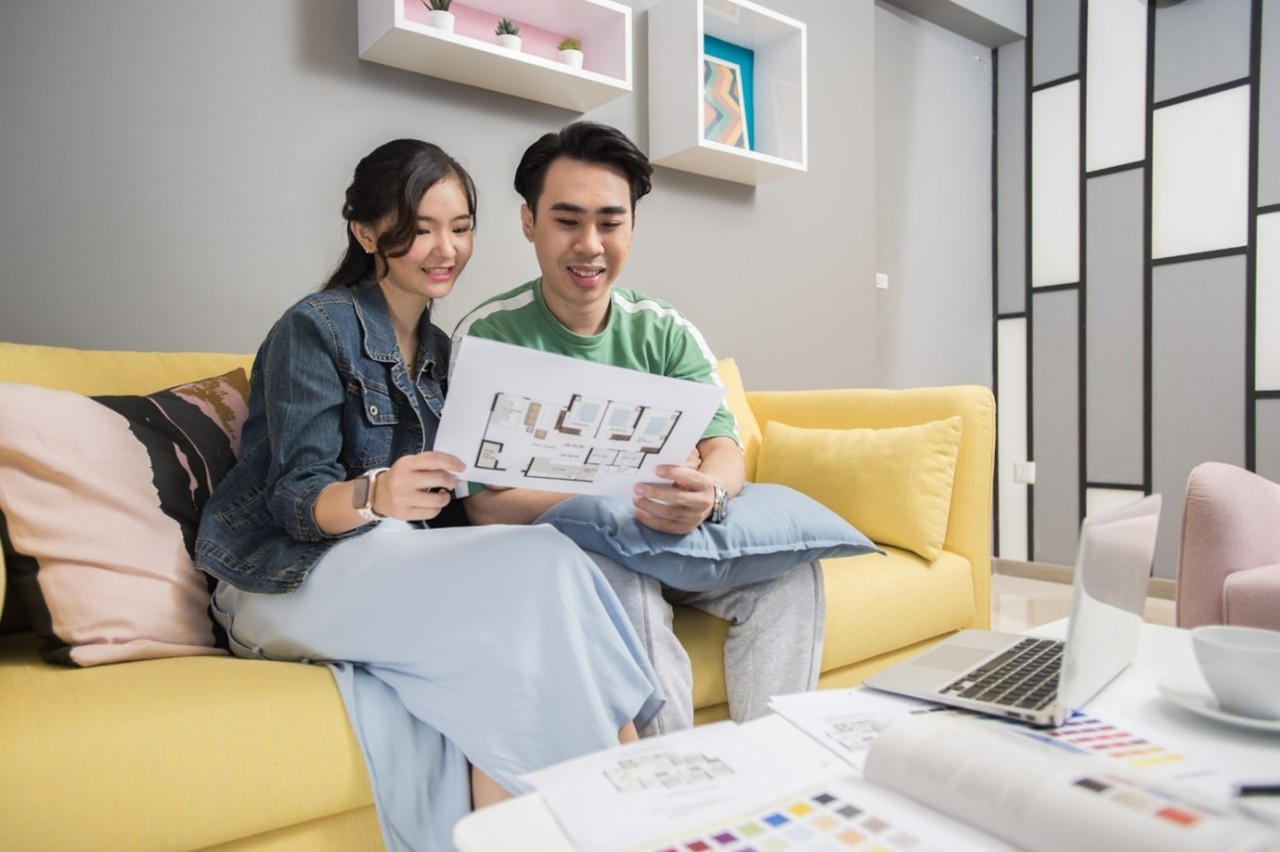 A family of 3 sheltered under a canvas that is held in the shape of a roof. 