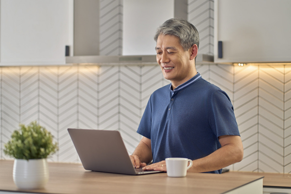 Senior man in his kitchen, looking at a laptop