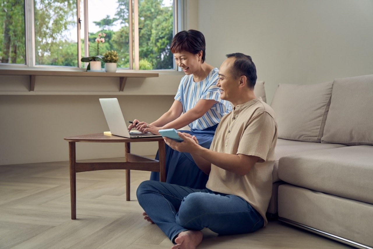 A couple using a calculator and a laptop each, smiling happily