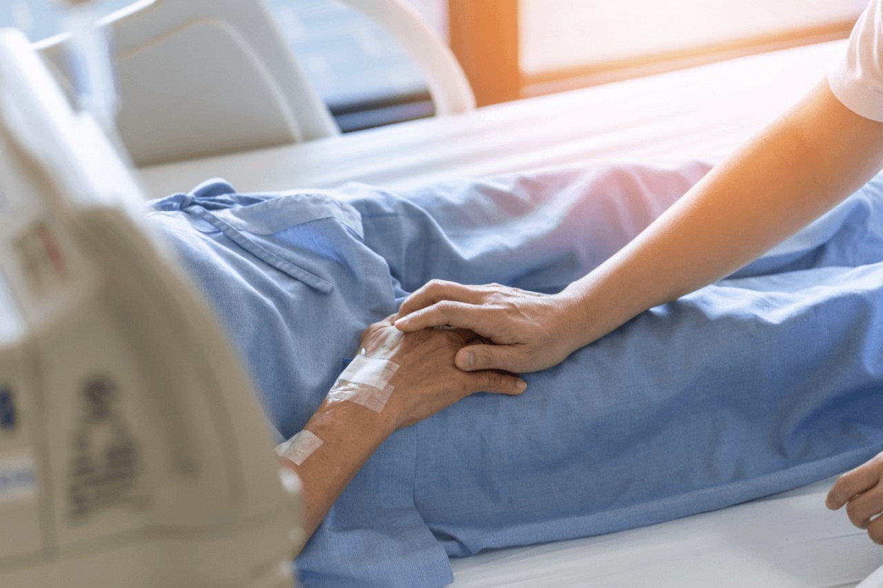 Caregiver holding elderly patient's hand in hospital bed