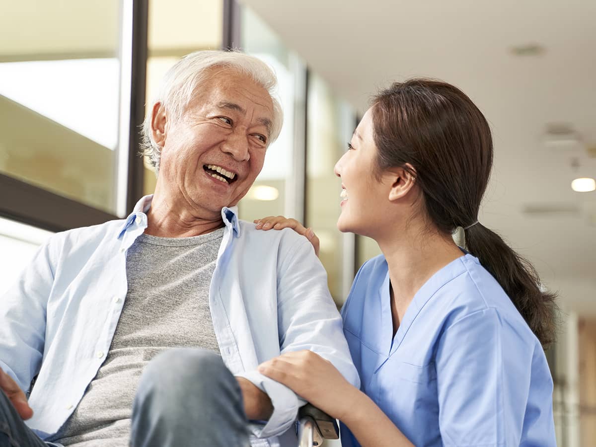 Young friendly Asian caregiver talks to elderly man in nursing home 