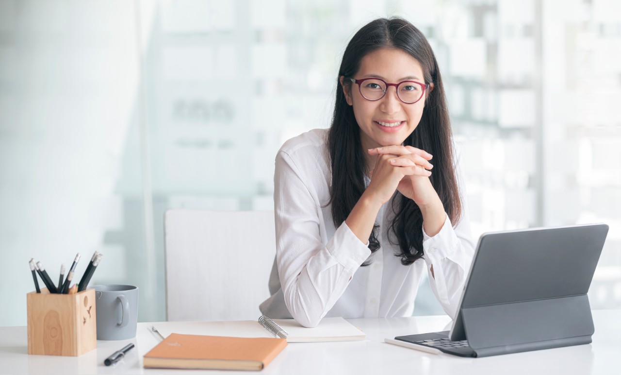 Picture of young asian women sitting at her office desk, relaxed and smiling at the camera