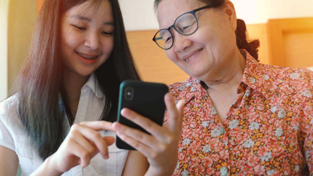 Asian lady helping her grandmother on her phone