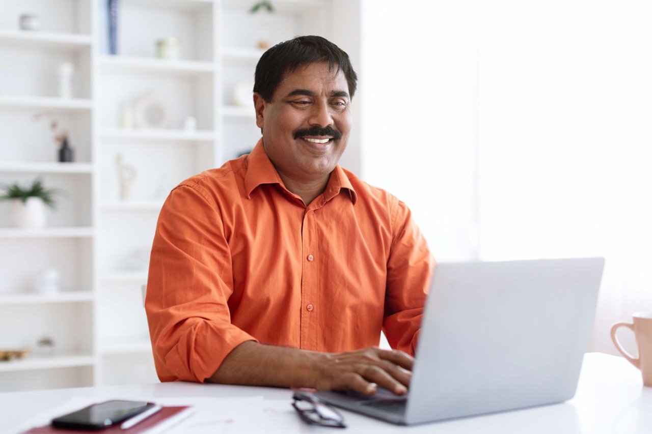 A smiling Indian man using laptop at home