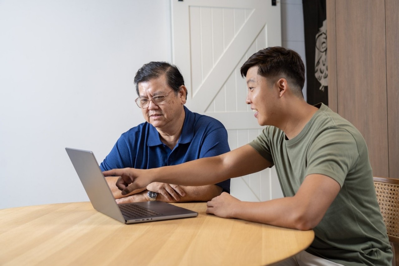 Young adult teaching senior how to use a laptop