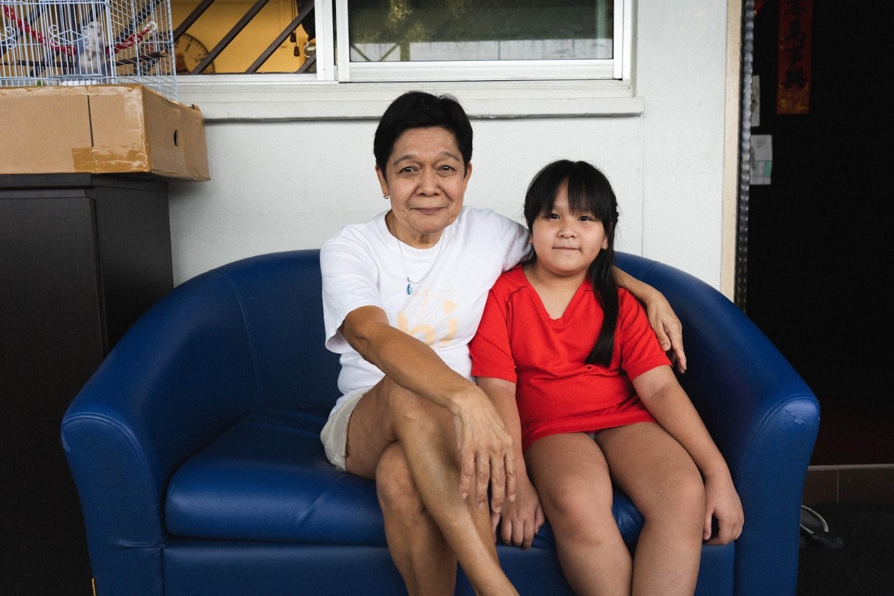 Beatrice and her granddaughter sitting on a sofa on their corridor.