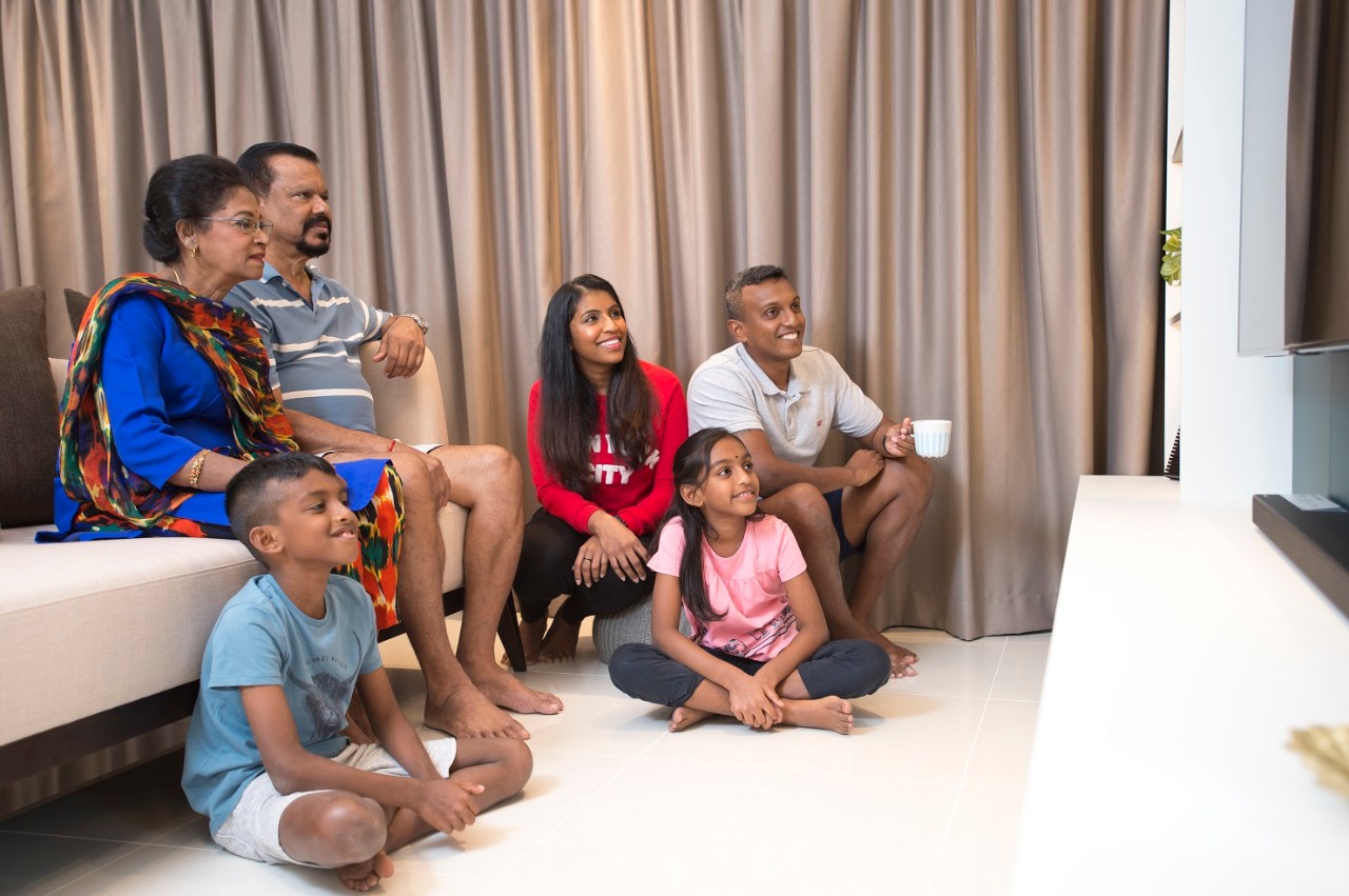 Asian Indian family of three generations seated in a living room and watching tv together 