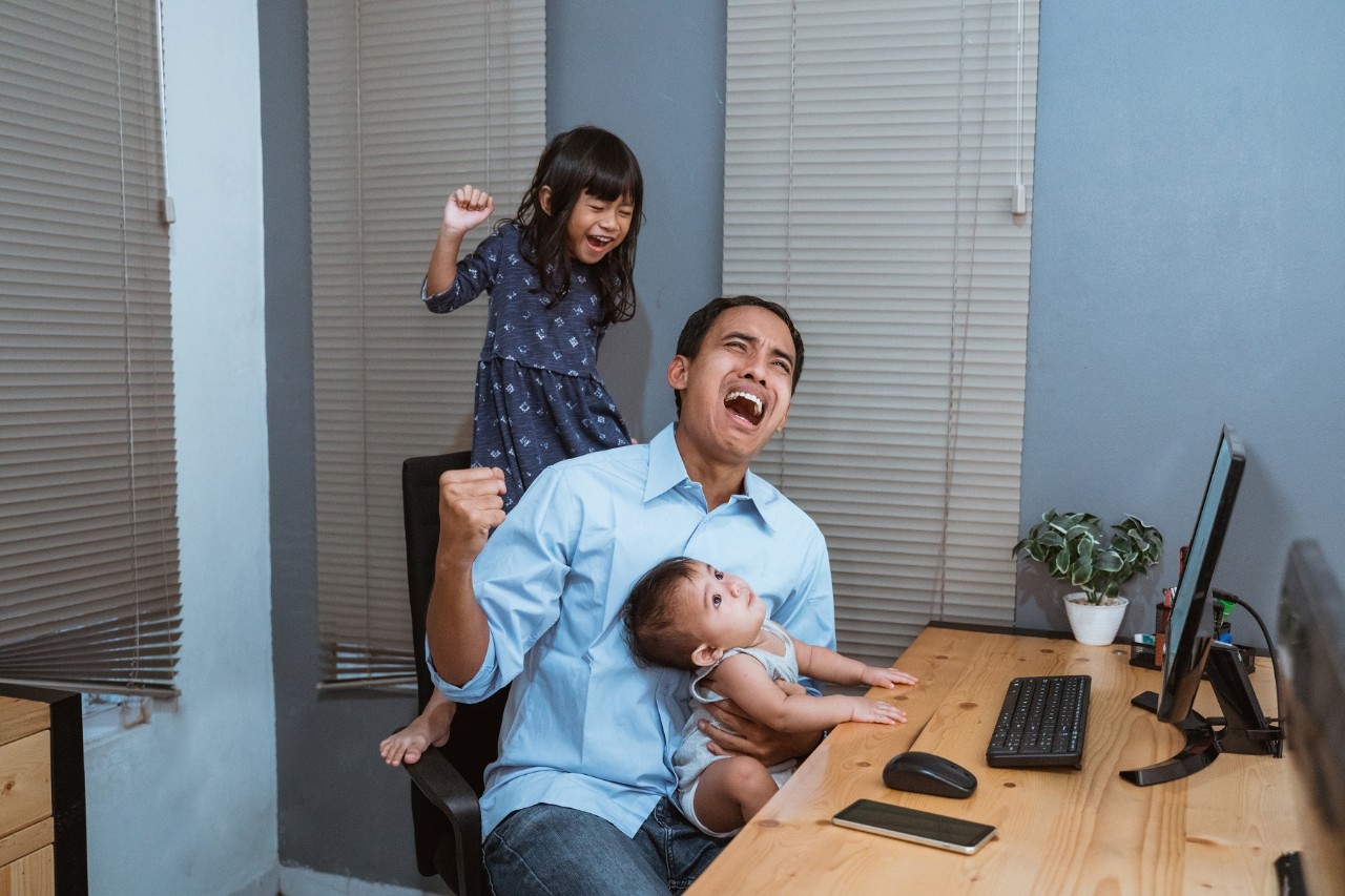 Father struggling to take care of two children, looking exasperated while working from home