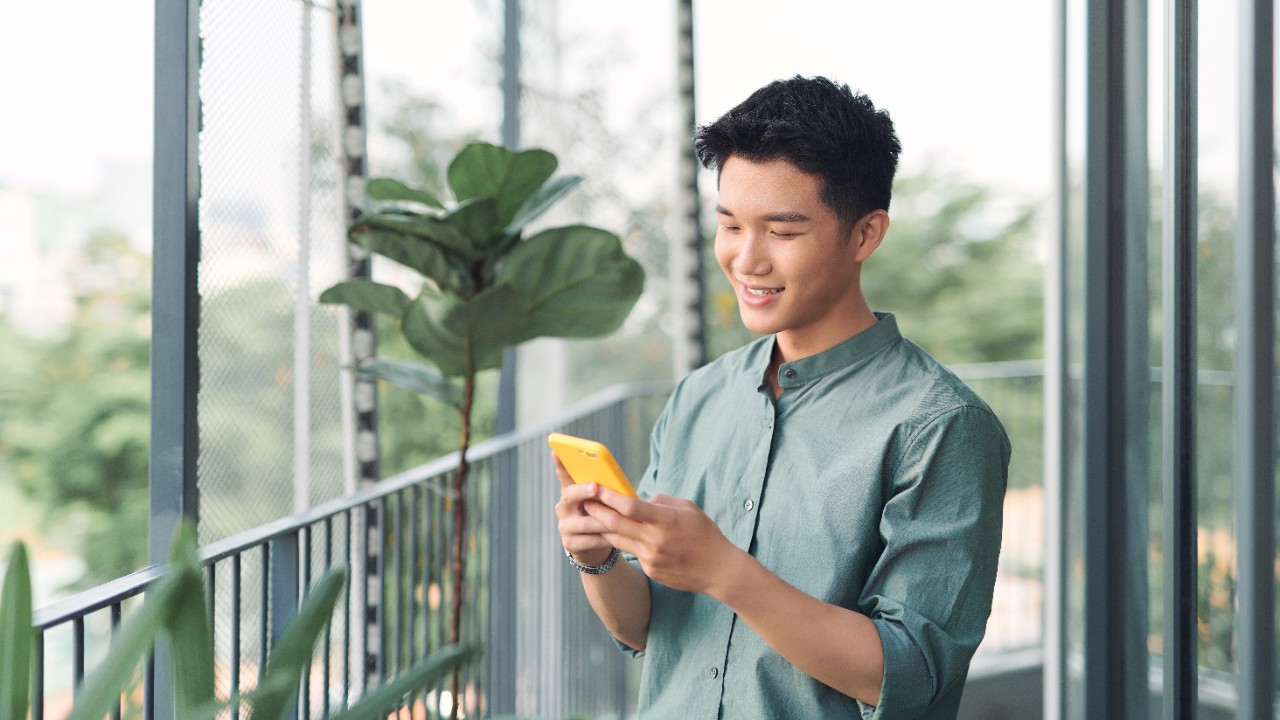 young asian man looking at his phone on the balcony