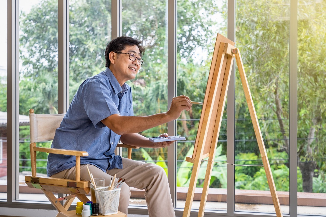 Senior smiling Asian man using brush and water color to paint on canvas